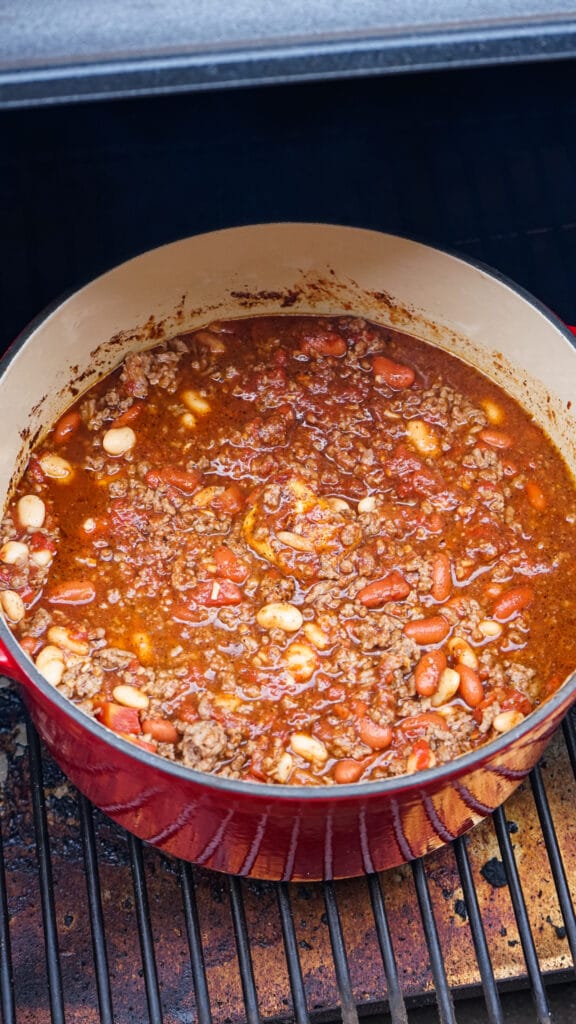 red dutch oven filled with chili in a smoker