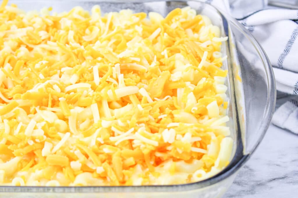 unbaked mac and cheese in a glass baking dish topped with shredded cheese