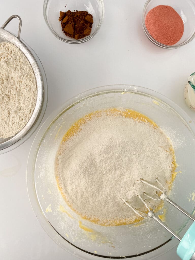flour being added to the wet ingredients in a glass mixing bowl