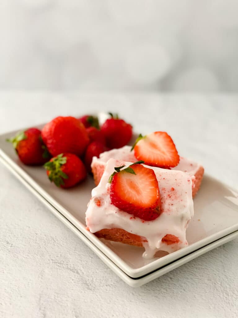 two strawberry blondies on a white platter with fresh strawberries