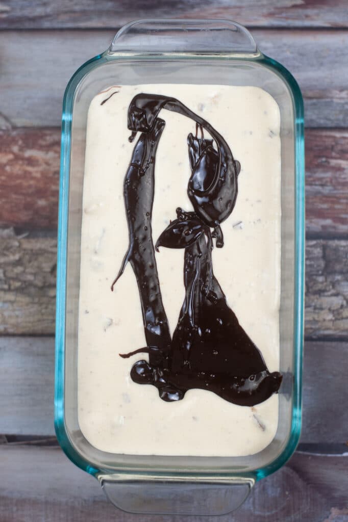 hot fudge being added to ice cream in a glass loaf pan