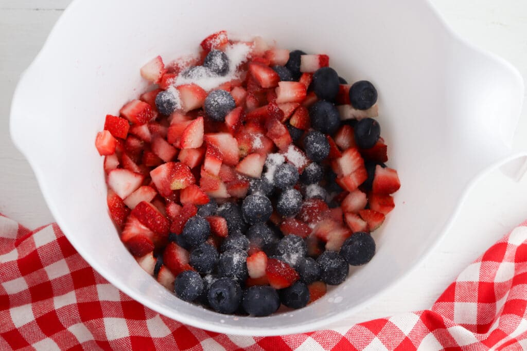 strawberries and blueberries in a white mixing bowl with sugar