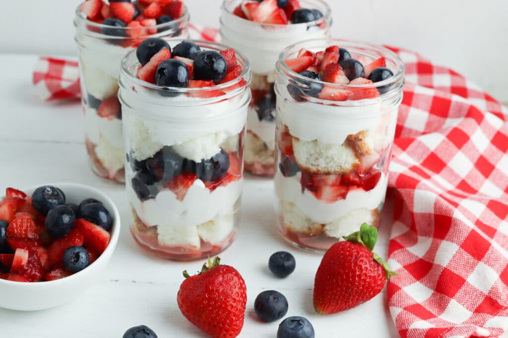 four jars of summer berry trifle on a wooden table with fresh berries