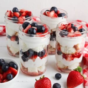 four jars of summer berry trifle on a white table