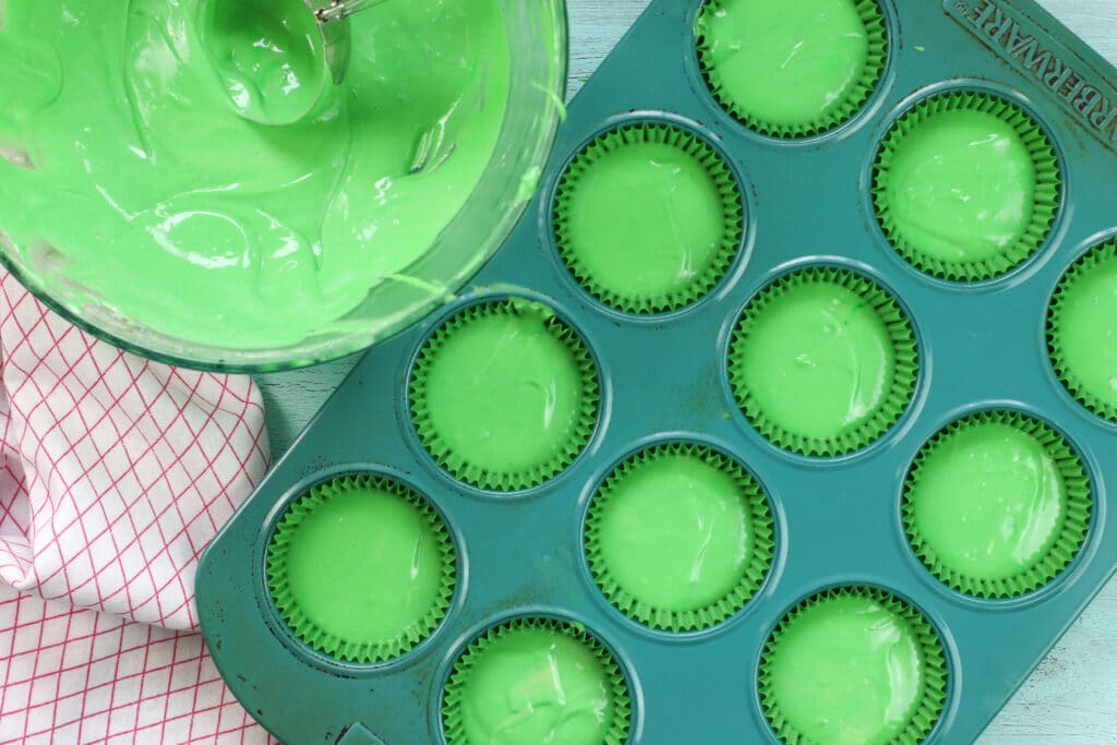 green cupcake batter being poured into cupcake liners