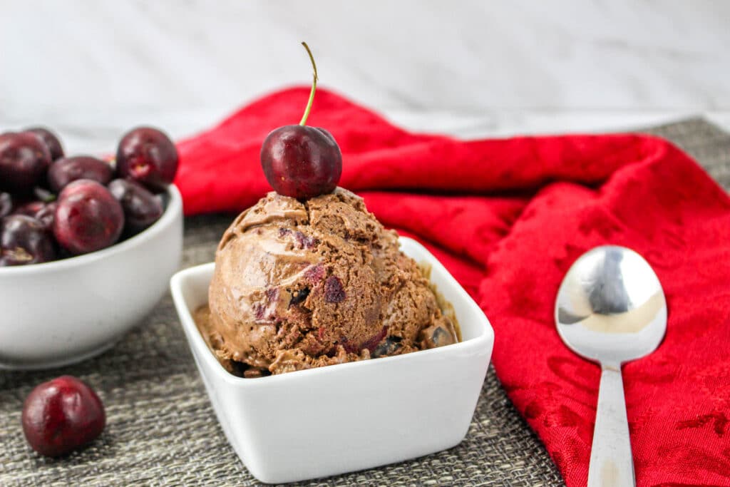 white bowl of black forest ice cream topped with a cherry
