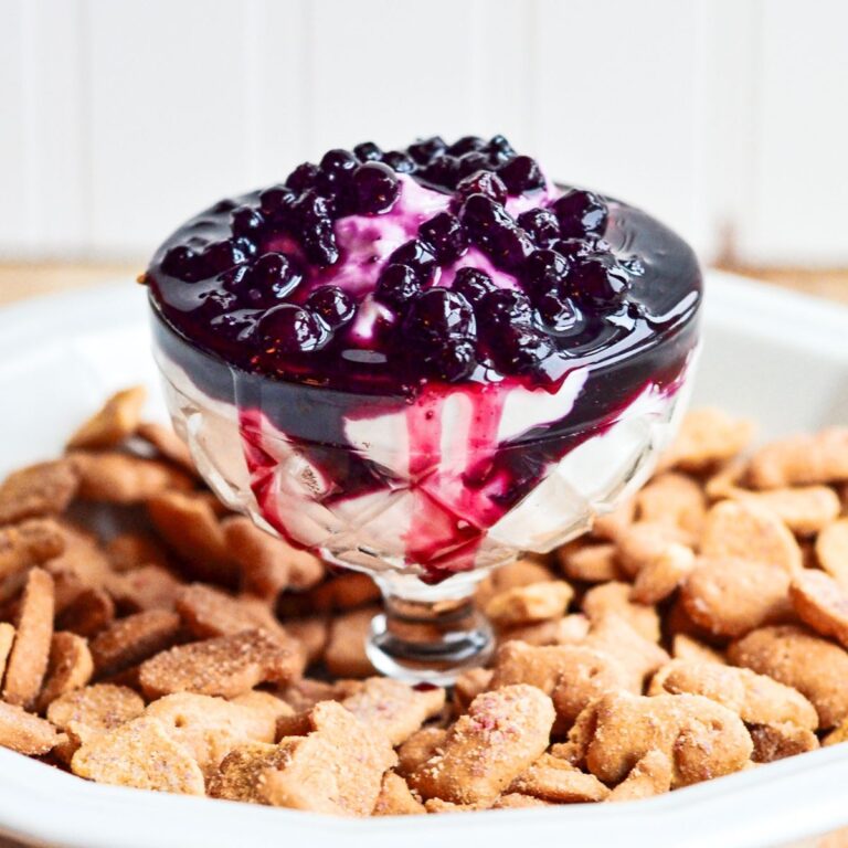 close up of a glass serving dish filled with blueberry cheesecake dip