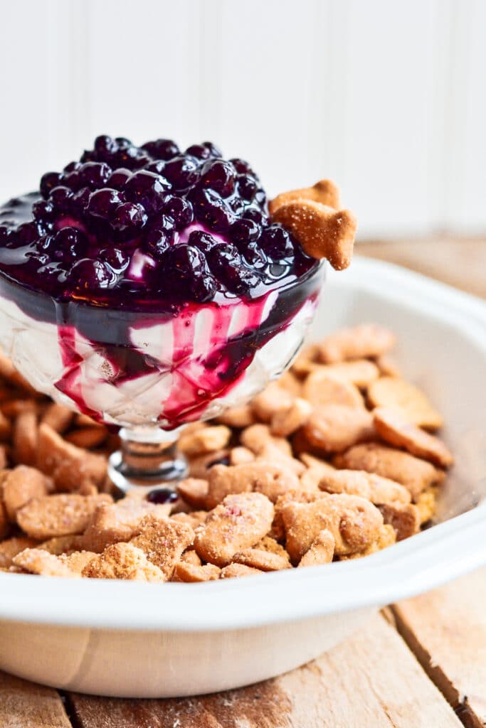 off center image Blueberry Cheesecake Dip in a glass bowl on top of a dish filled with graham crackers