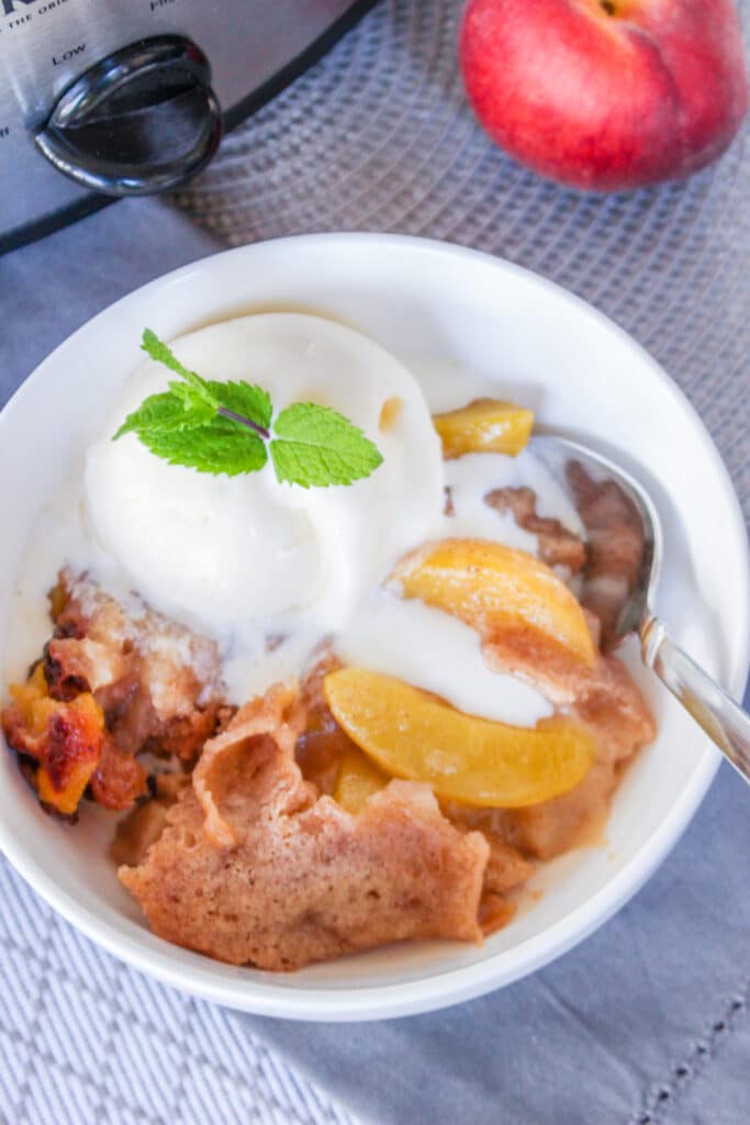 off center image of a white bowl filled with slow cooker peach cobbler