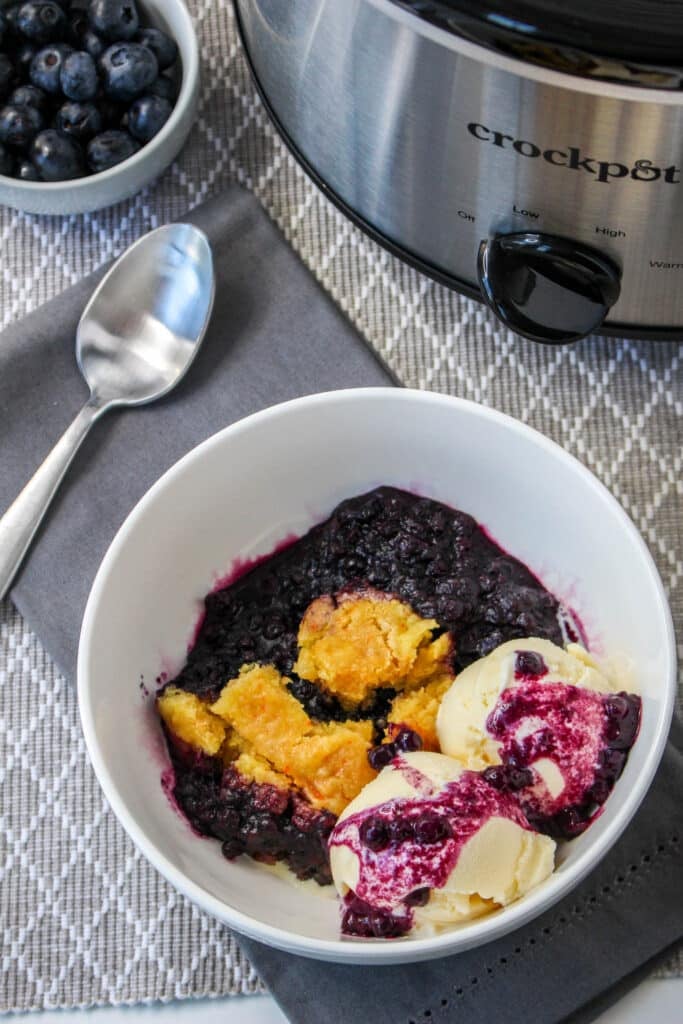 birds eye image of a bowl filled with slow cooker blueberry cobbler topped with ice cream