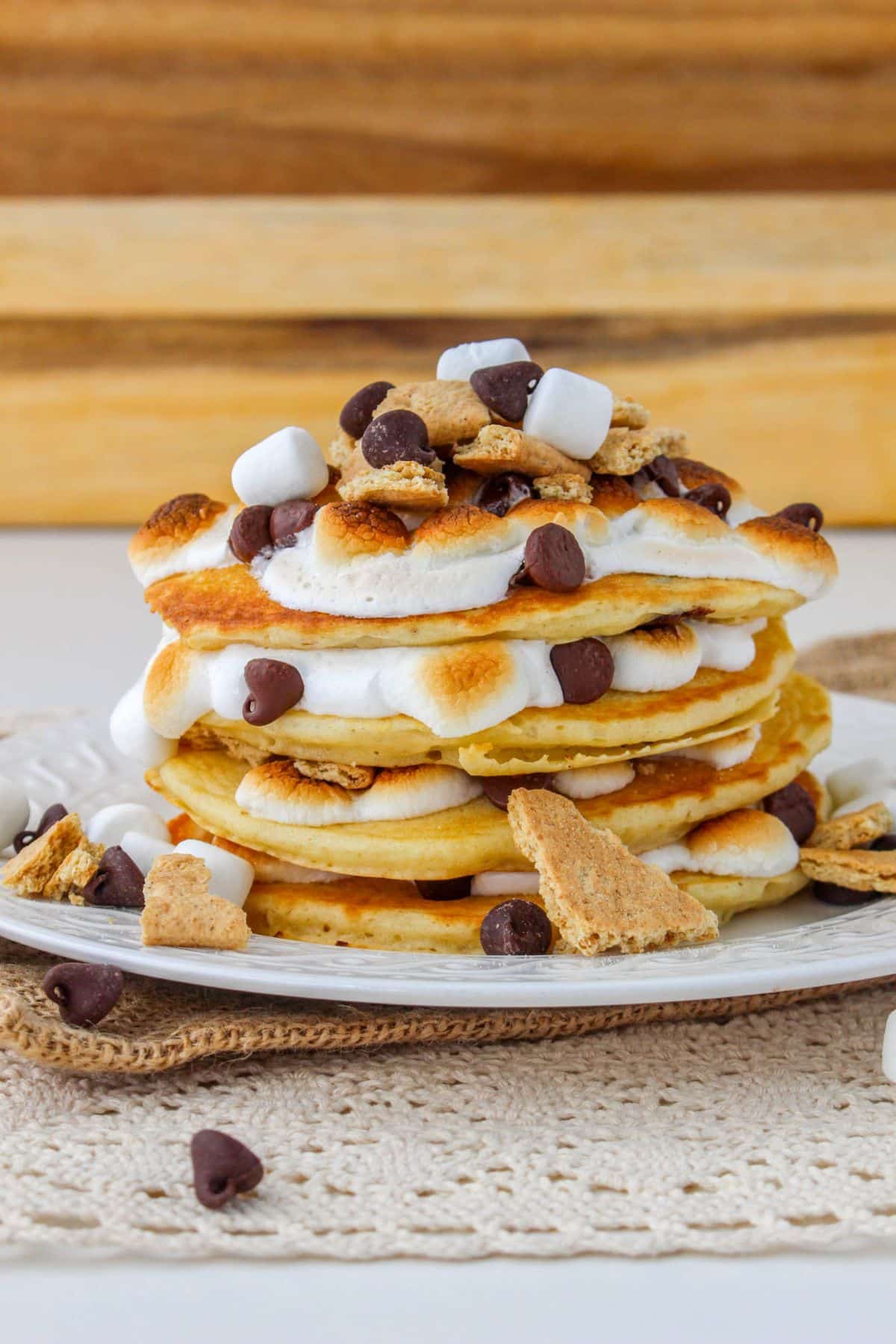 stack of smores pancakes on a white plate with a wooden background
