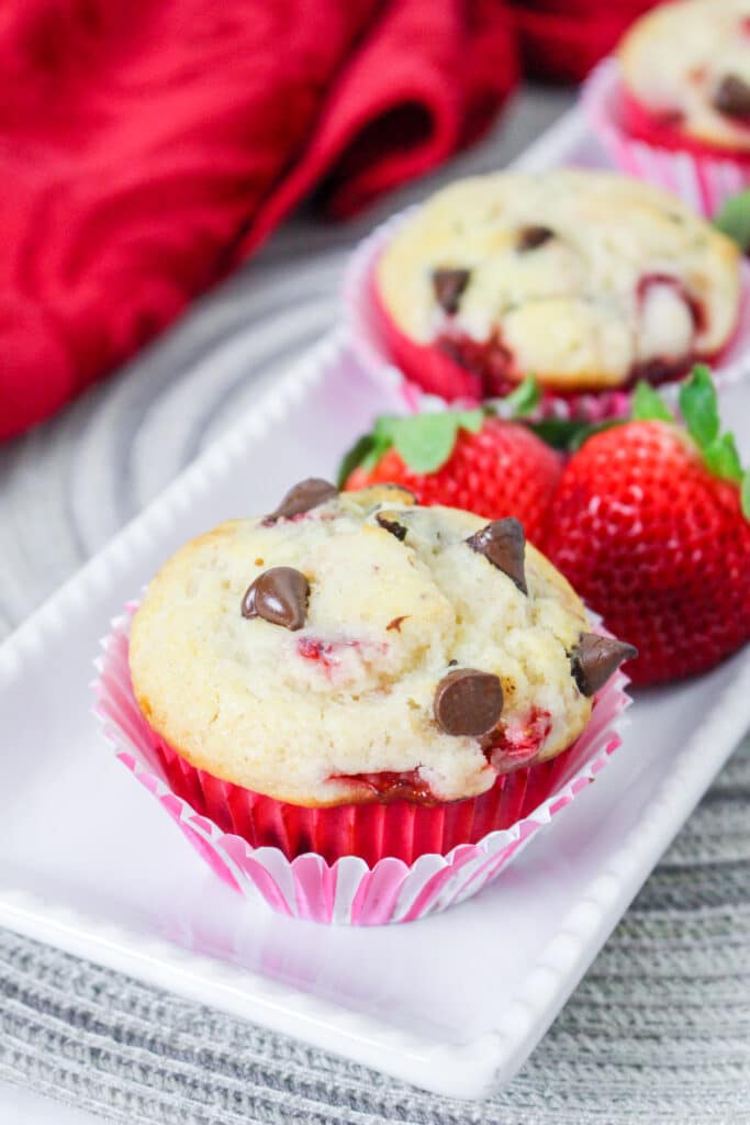 strawberry chocolate chip muffins on a white platter with fresh strawberries