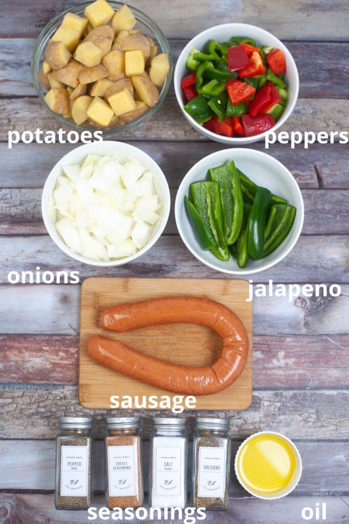 potatoes, peppers, onions, jalapeno, sausage, seasonings and oil on a wooden background
