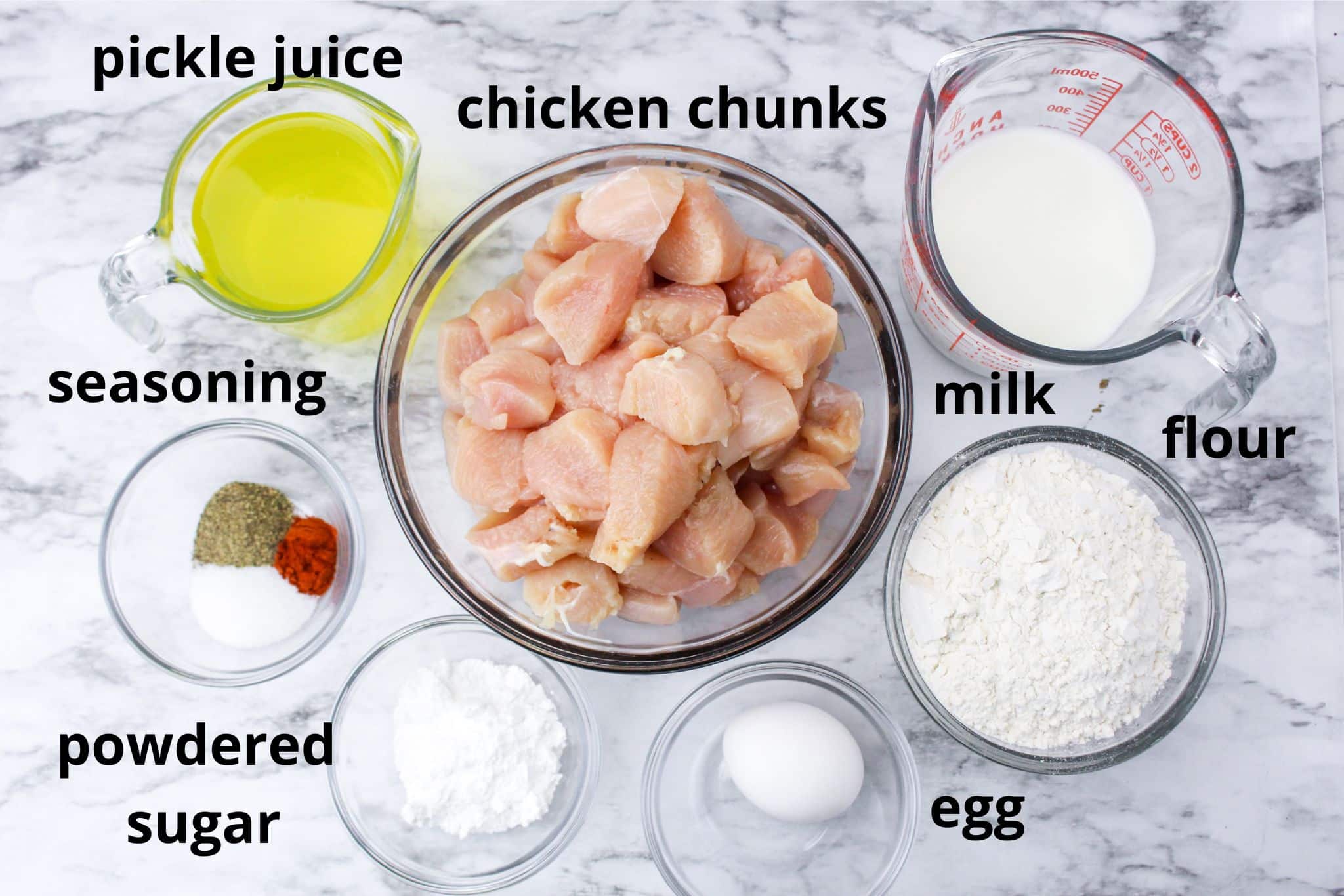 pickle juice, chicken chunks, milk, flour, seasoning, powdered sugar, egg on a marble counter