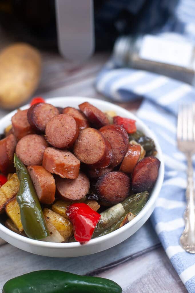 off center image of air fryer kielbasa and vegetables in a white bowl