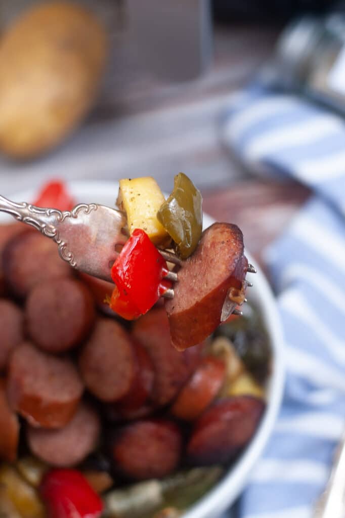 Sausage, peppers, and a potato on a fork held in the air