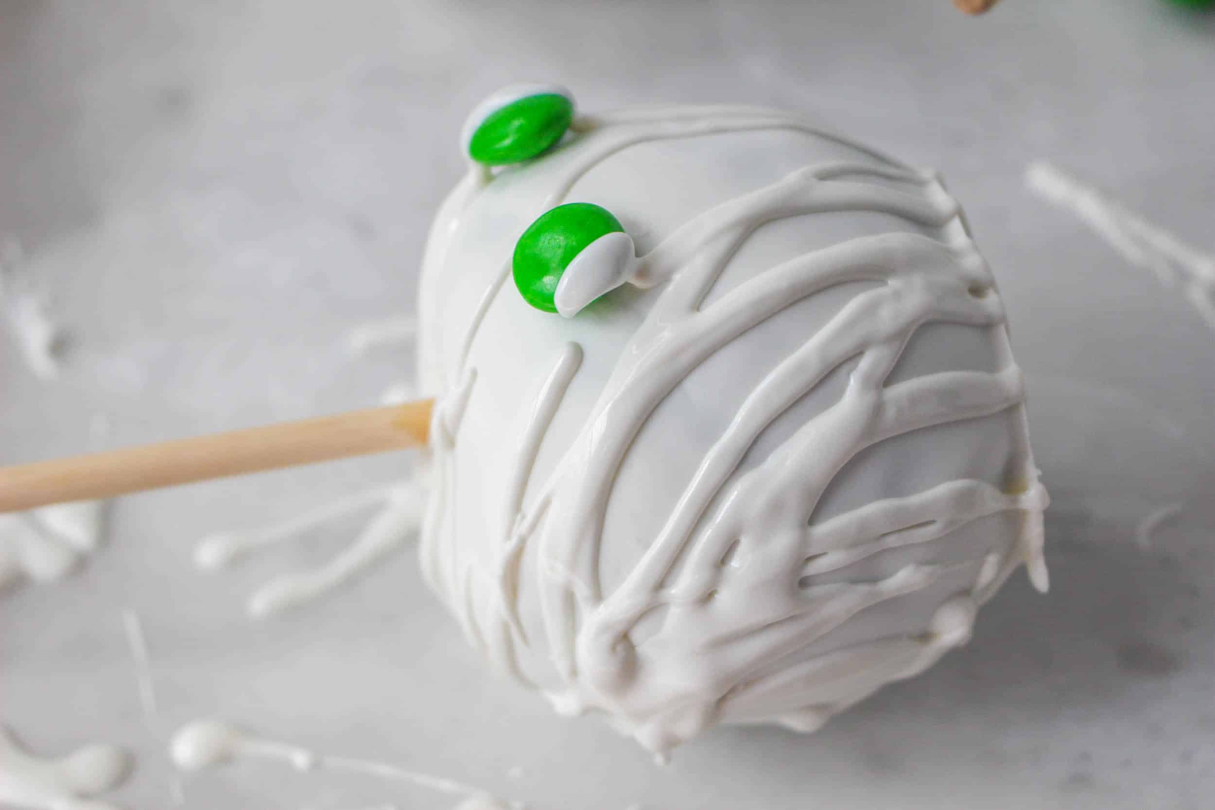 white chocolate coated apple on it's side with green candy being stuck on it