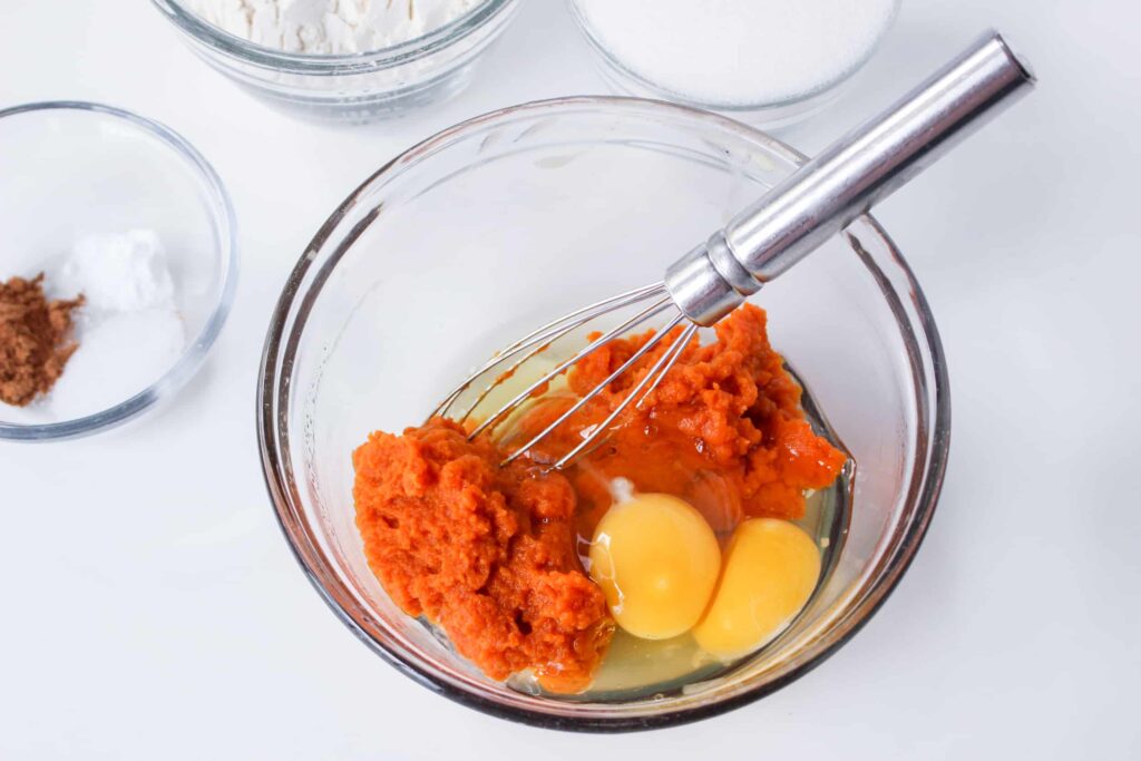 pumpkin and eggs in a glass mixing bowl with a whisk