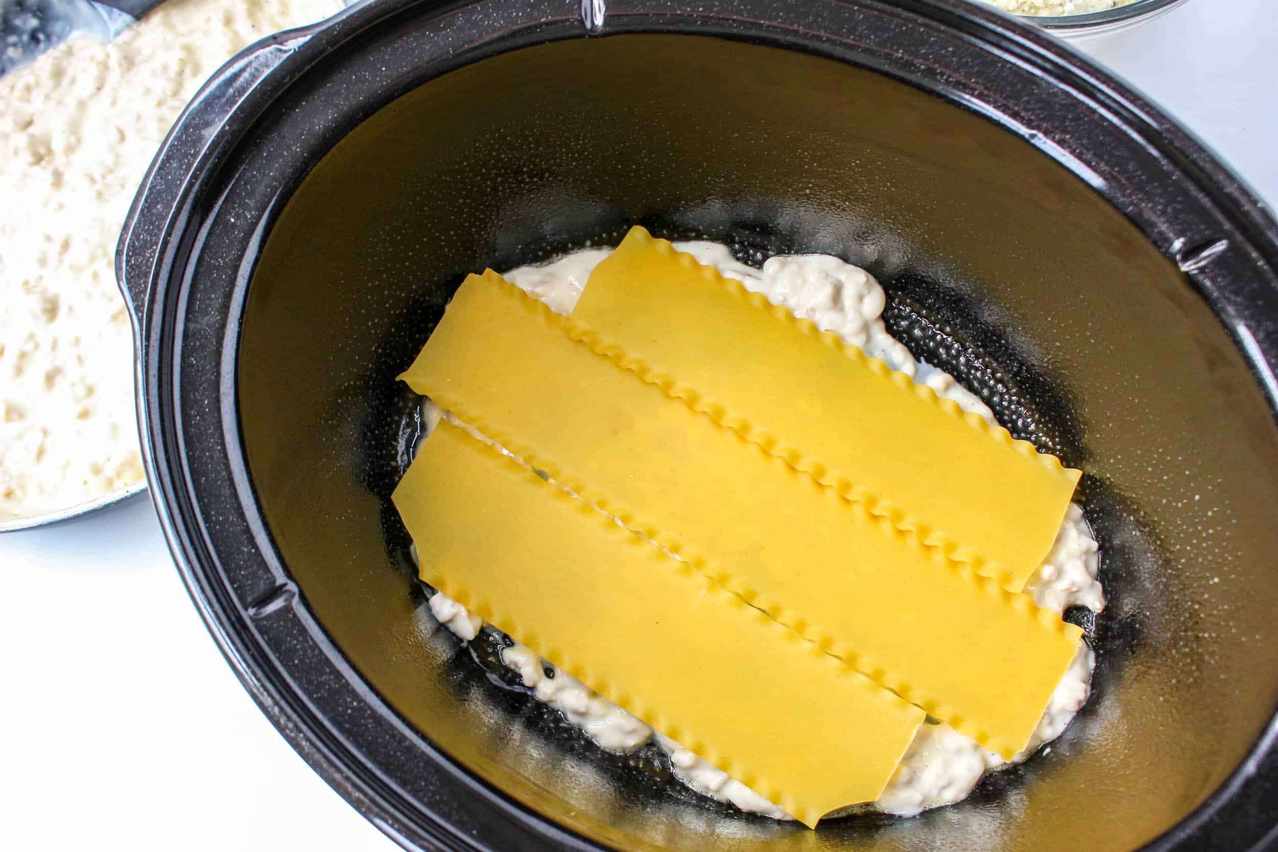 raw lasagna noodles on top of the alfredo sauce in a crock pot