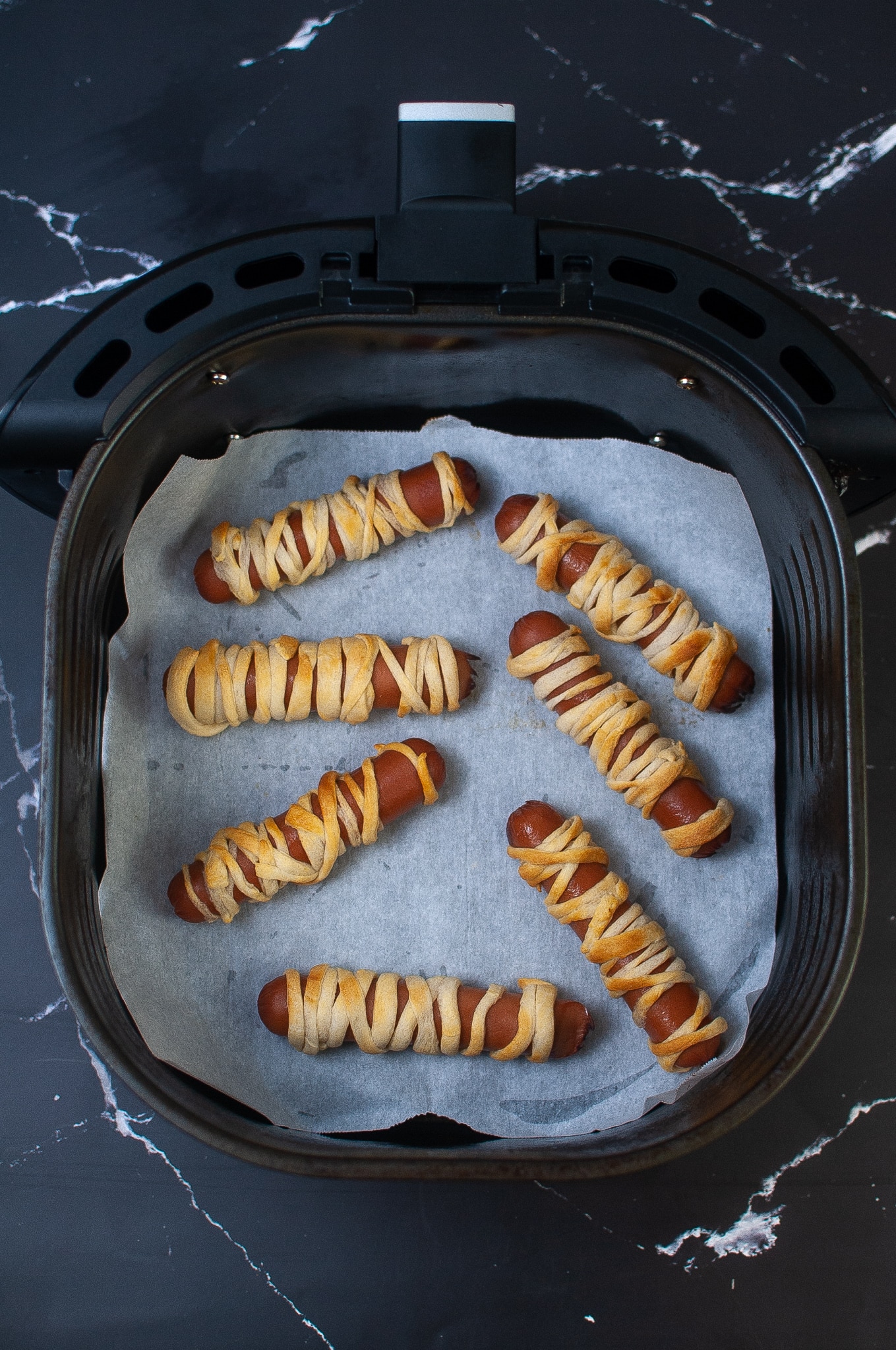 cooked dogs in an air fryer basket lined with parchment paper