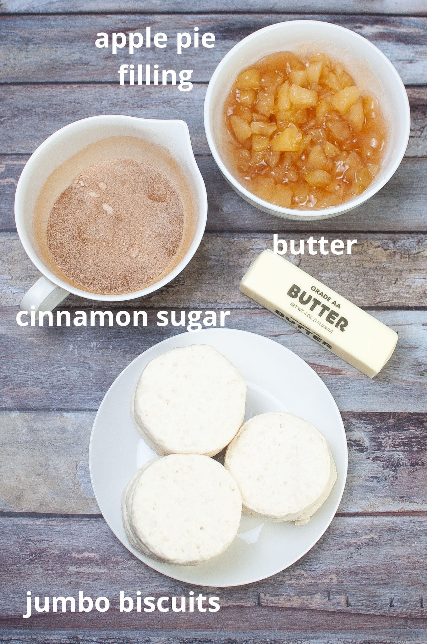 bowls of cinnamon sugar, apple pie filling, butter and jumbo canned biscuits on a wooden background