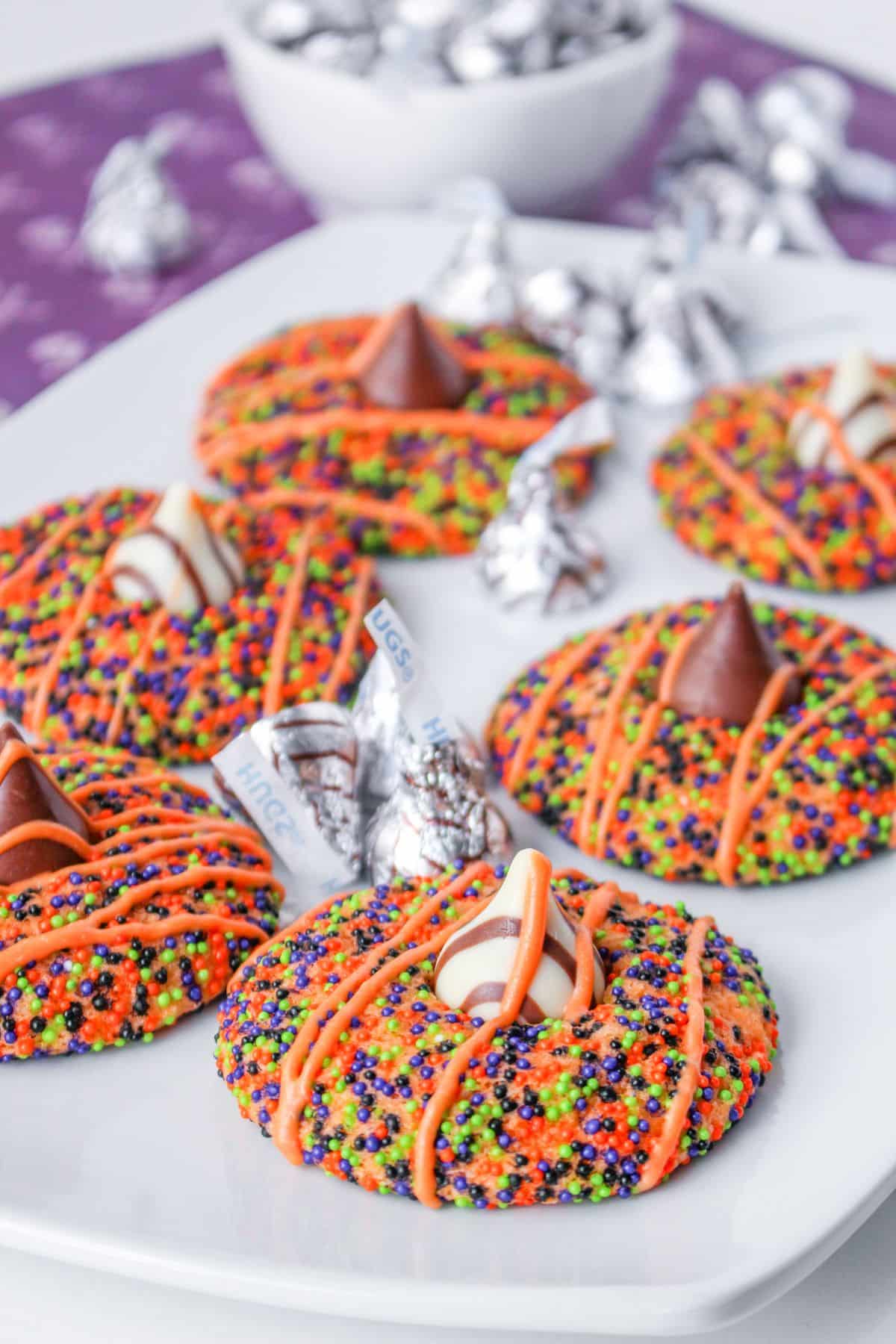 six halloween sprinkle cookies on a white plate with hershey kisses