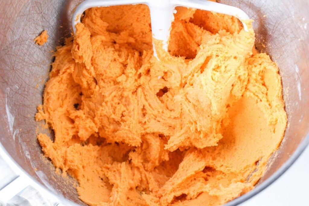 orange cookie dough in a stainless steel mixing bowl