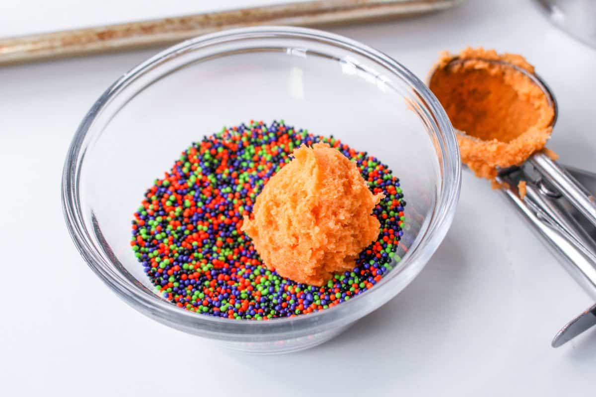 ball of cookie dough being rolled in a bowl of sprinkles