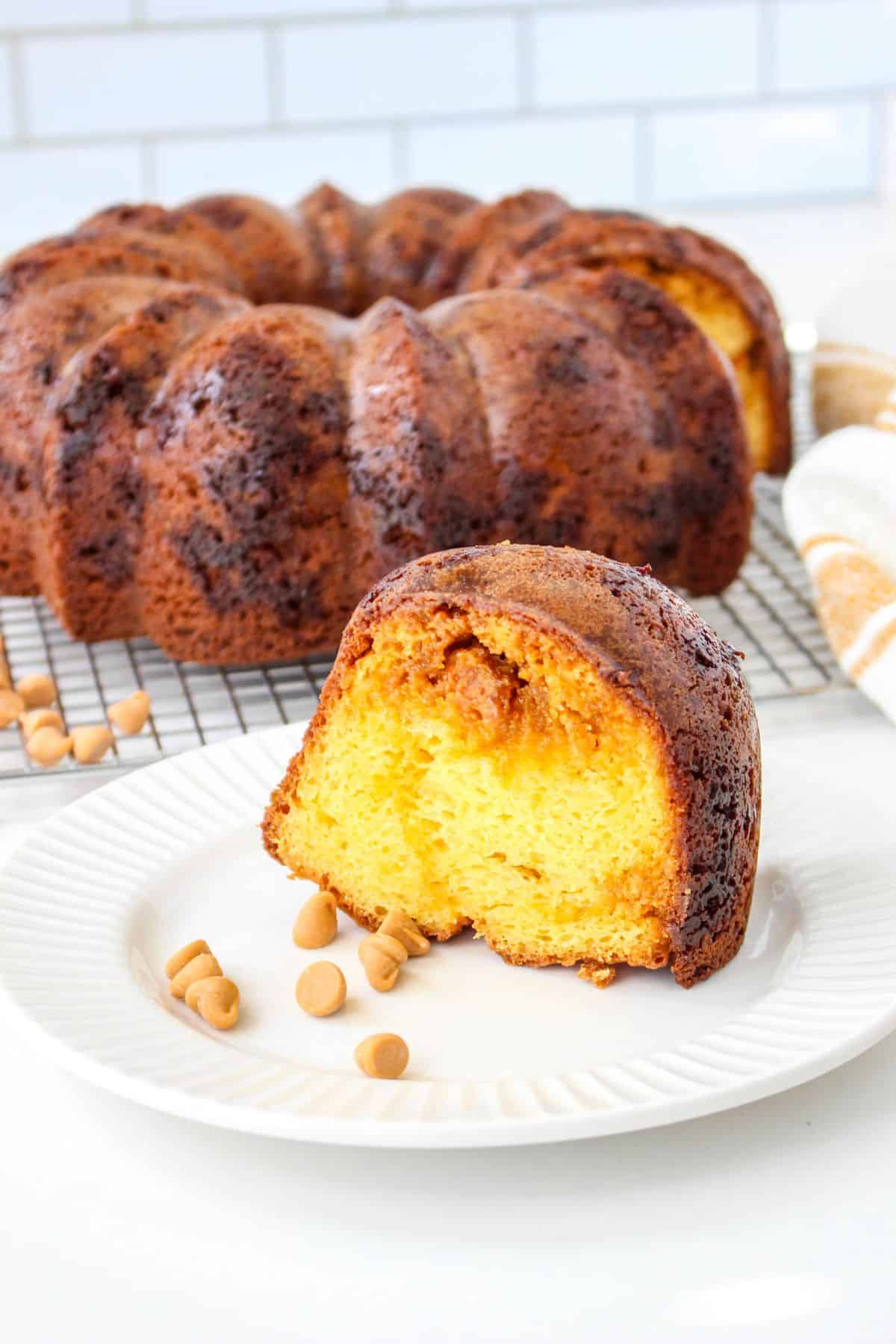 slice of butterscotch budnt cake on a white plate with the whole cake behind it.