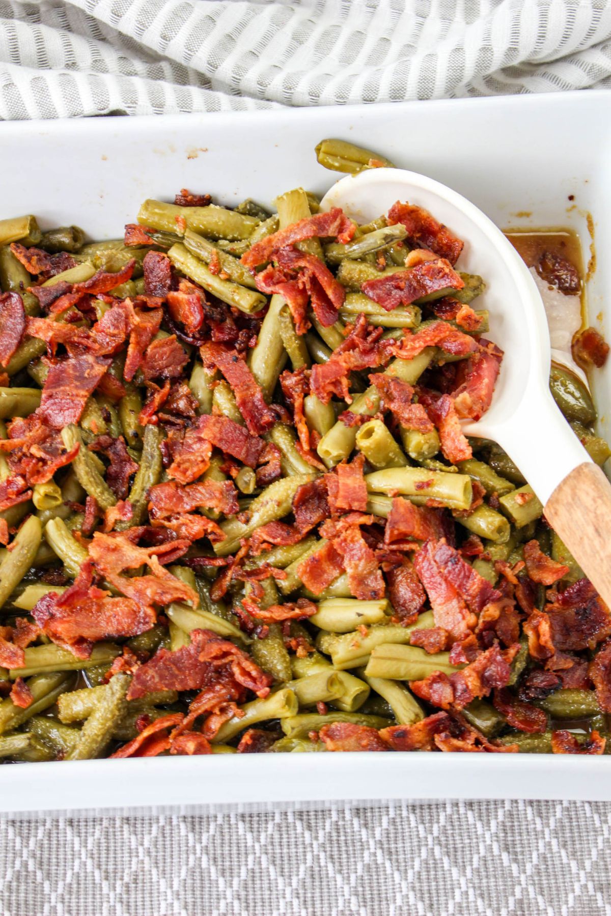 cooked crack green beans in a white casserole dish with a wooden spoon
