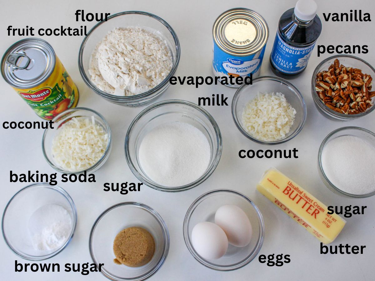 flour, fruit cocktail, vanilla, pecans, evapoated milk, coconut, sugar, butter, eggs, brown sugar, and baking soda on a white background