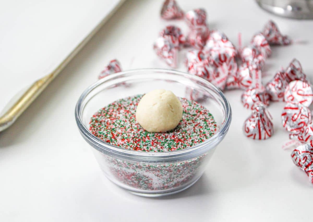 cookie dough ball being rolled in red, white and green sprinkles