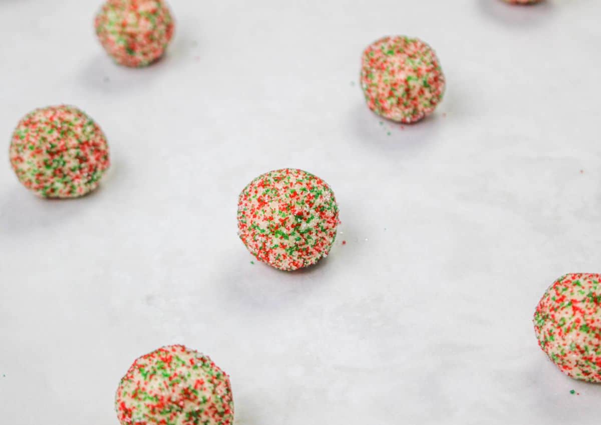 cookie dough balls rolled in sprinkles on a parchment lined baking sheet