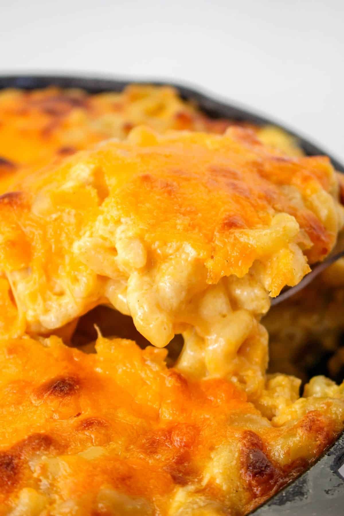 a scoop of mac and cheese being removed from a cast iron skillet