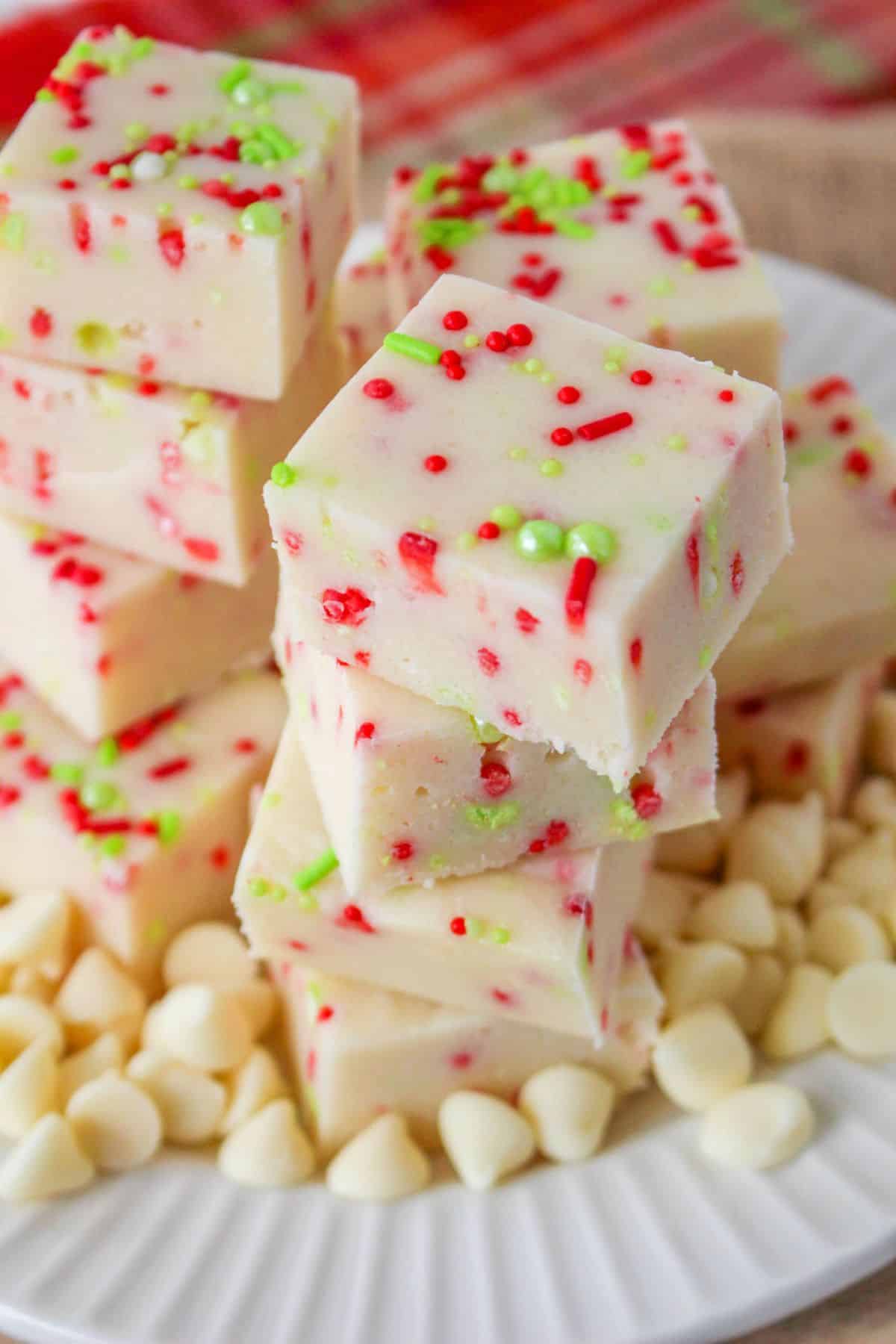 christmas cookie fudge stacked on a white plate surround by white chocolate chips