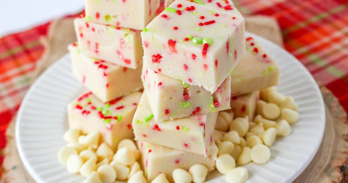 christmas cookie fudge stacked on a white plate surround by white chocolate chips