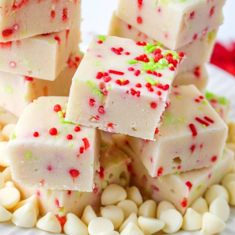 christmas cookie fudge stacked on a white plate surround by white chocolate chips