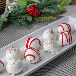 10 christmas tree cake balls on a rectangle white plate iwth holly in the background