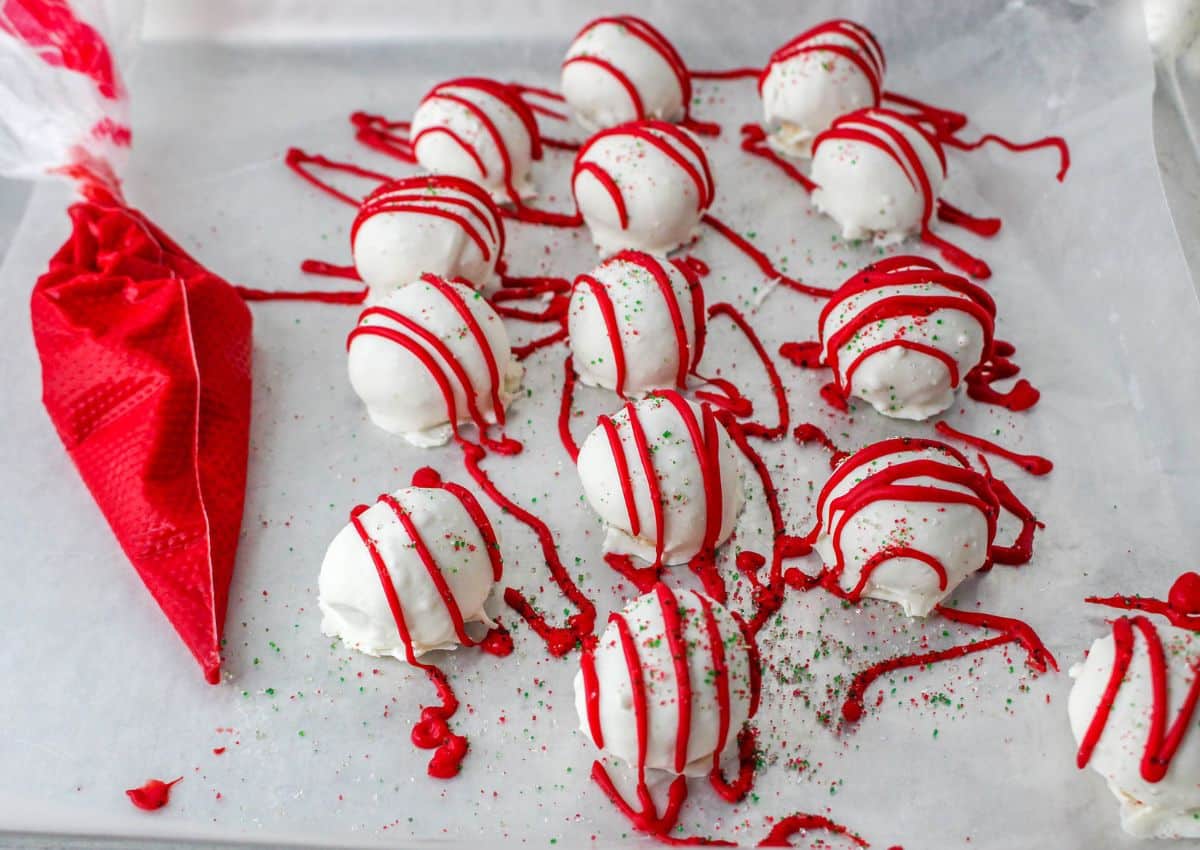 christmas tree cake balls on parchment lined baking sheet with red candy melts drizzled on the top