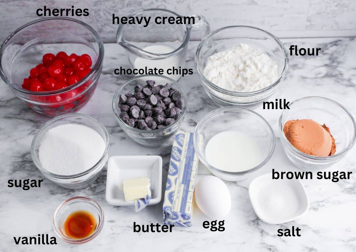cherries,heavy cream, chocolate chips, flour, milk, brown sugar, salt, egg, butter, vanilla, and sugar on a marble backdrop