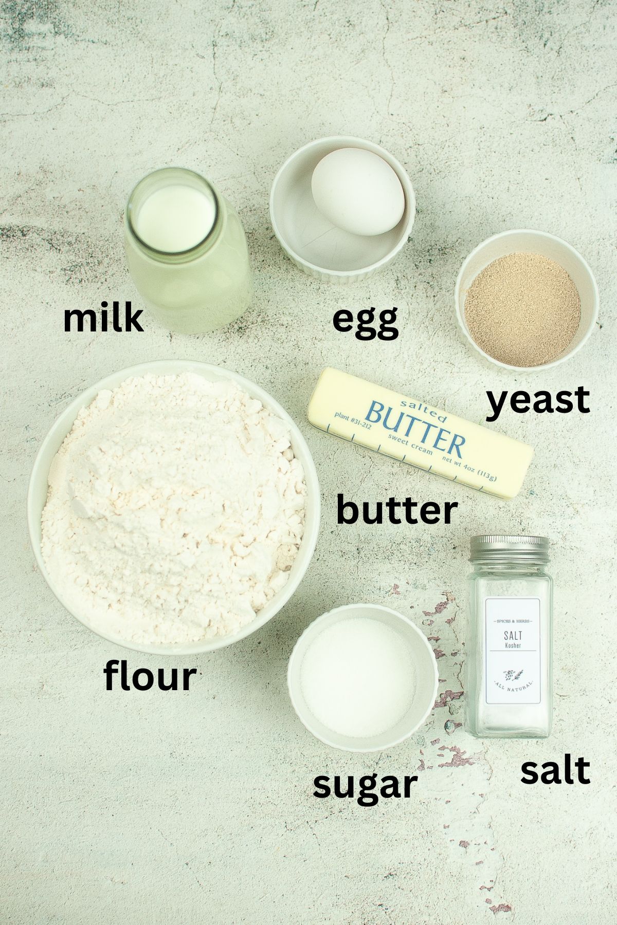 milk, egg, yeast, butter, flour, sugar, and salt on a textured background
