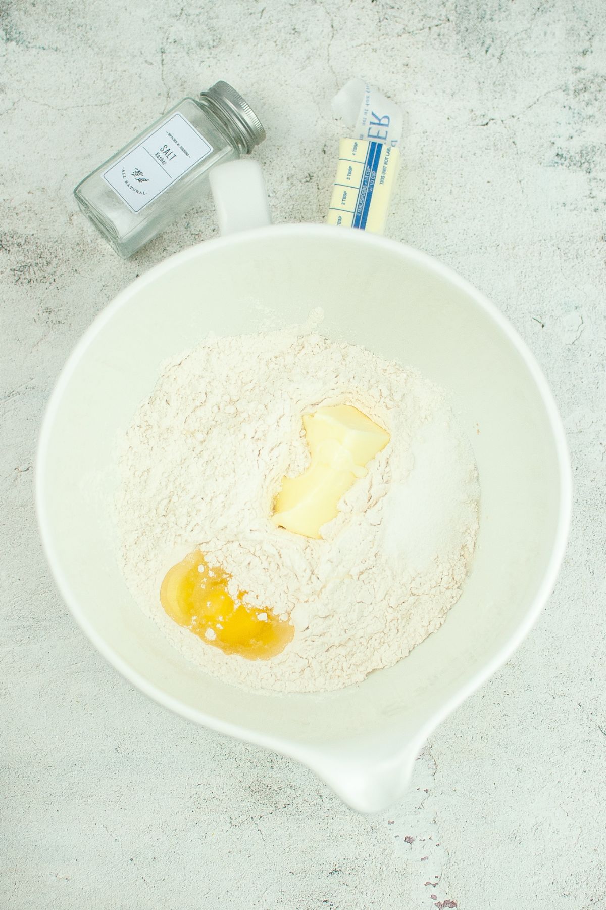 eggs, butter and flour in a white mixing bowl on a textured background
