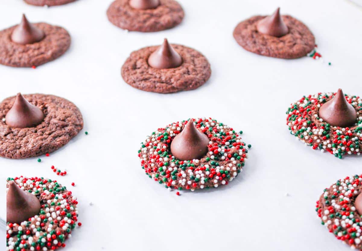 baked cookies being topped with a hershey kiss on a parchment lined baking sheet