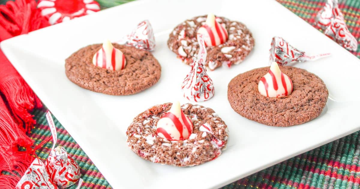 four chocolate peppermint kiss cookies on a white plate with candy cane kisses
