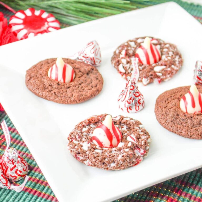 four chocolate peppermint kiss cookies on a white plate with candy cane kisses