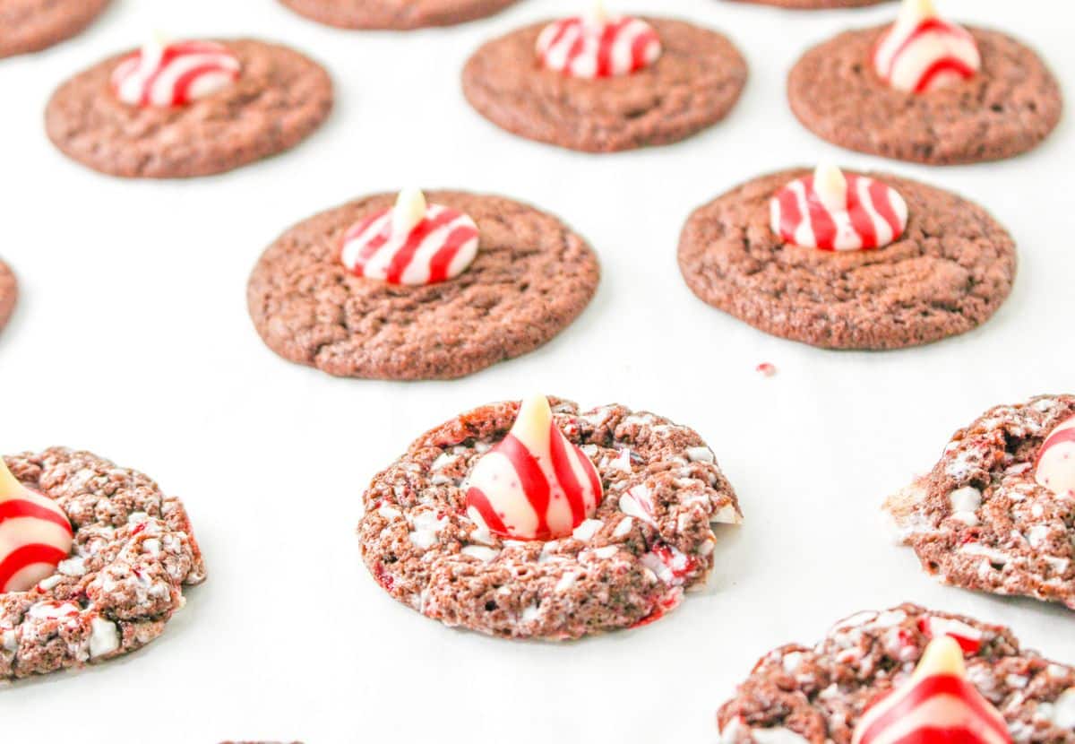 baked cookies being topped with candy cane hershey kiss on a parchment lined baking sheet
