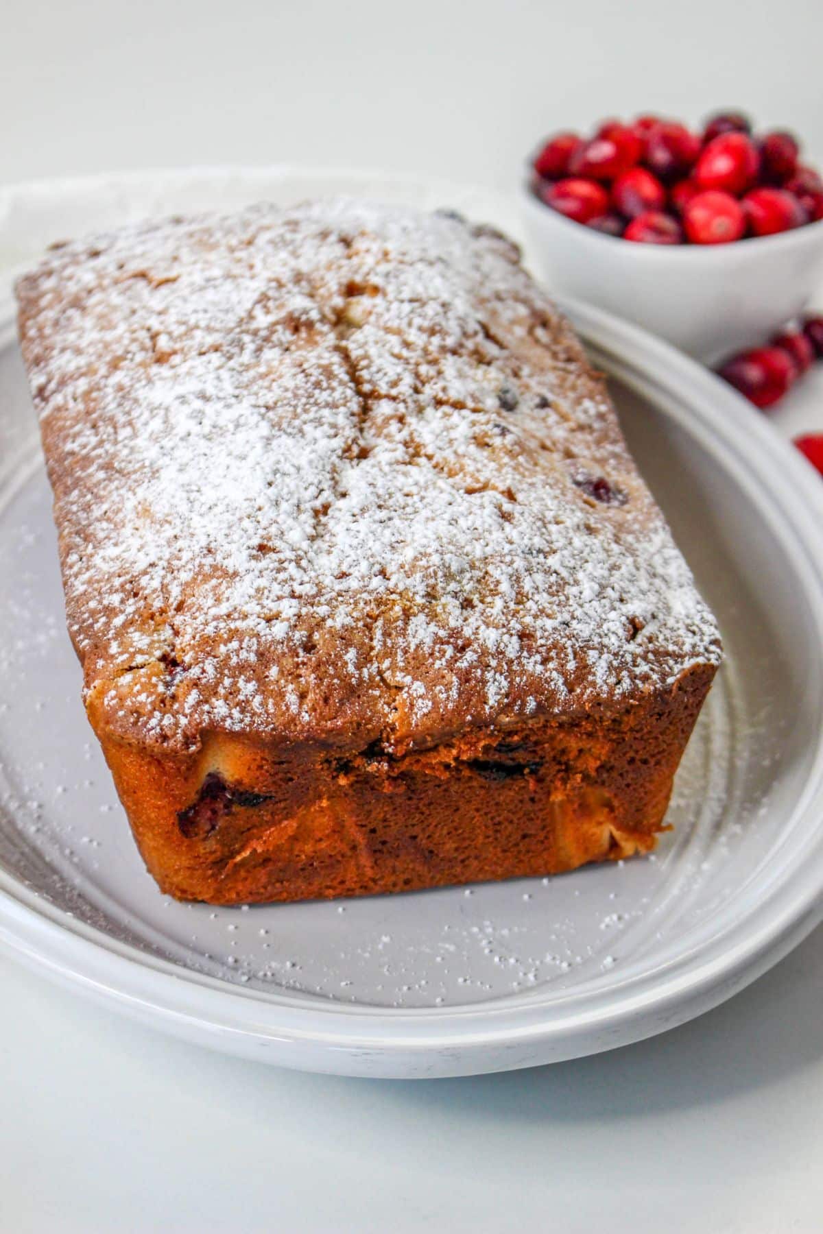 uncut christmas cranberry pound cake dusted with powdered sugar on a white serving platter