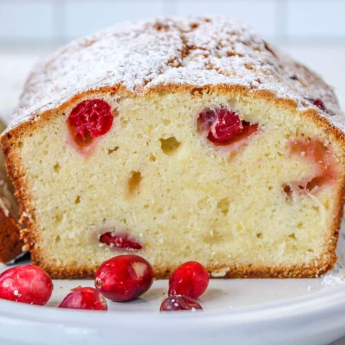 slice of christmas cranberry pound cake on a white plate with a few fresh cranberries