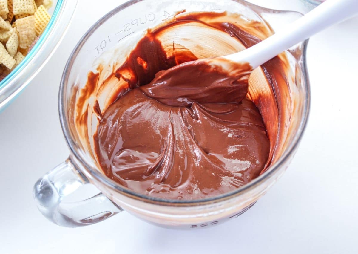 melted chocolate in a glass mixing bowl with a white plastic spoon