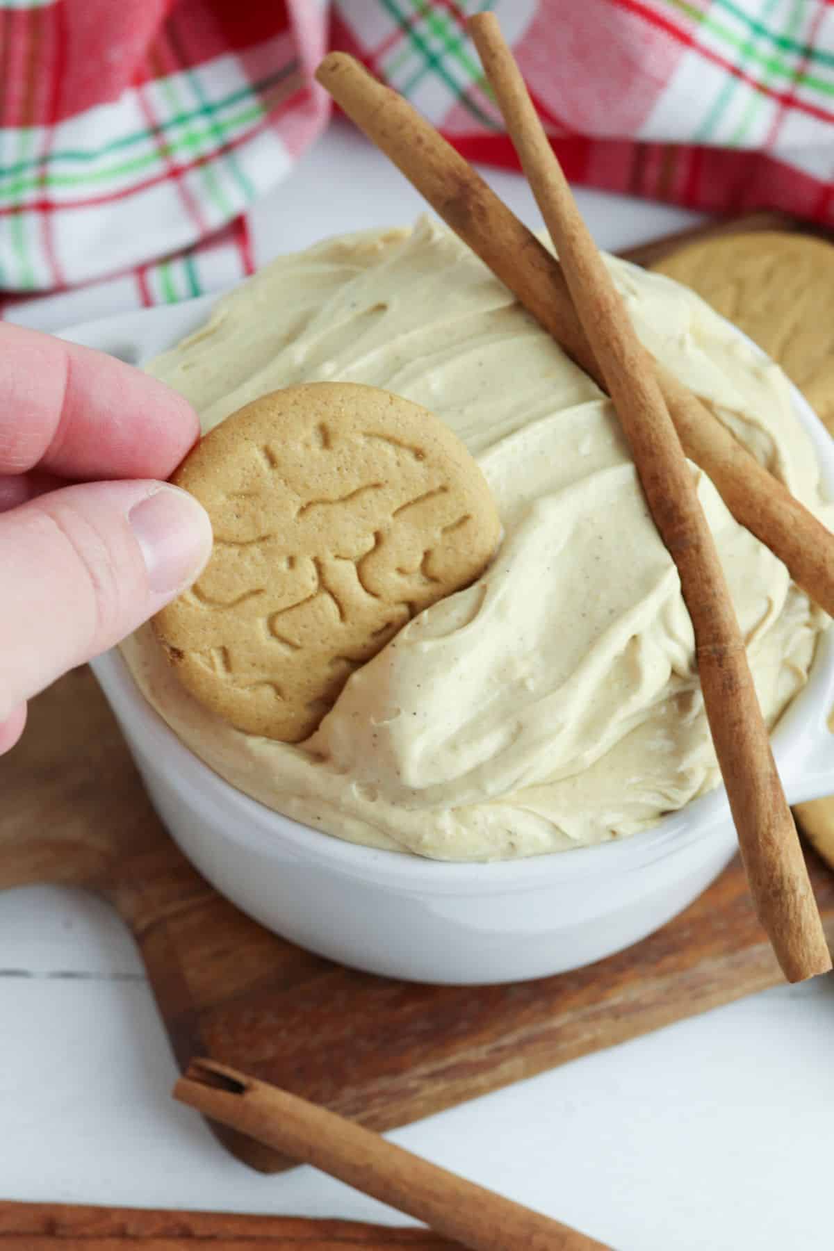 white bowl filled with gingerbread dip topped with cinnamon sticks with a cookie being dipped in it